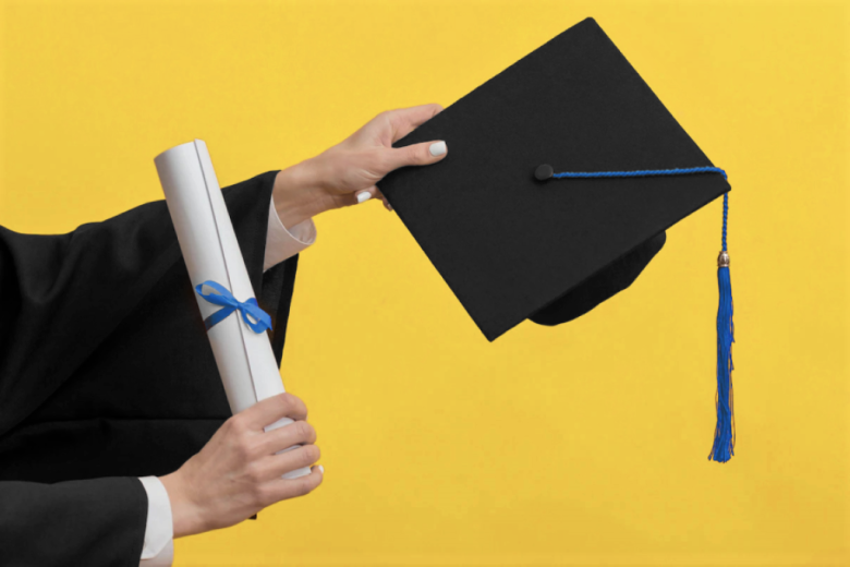 ręce trzymają dyplom absolwenta uczelni i biret 