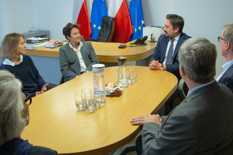 Marcin Wiącek i Hanna Machińska rozmawiają z gośćmi przy stole w gabinecie rzecznika. W tle flagi Polski i Unii Europejskiej