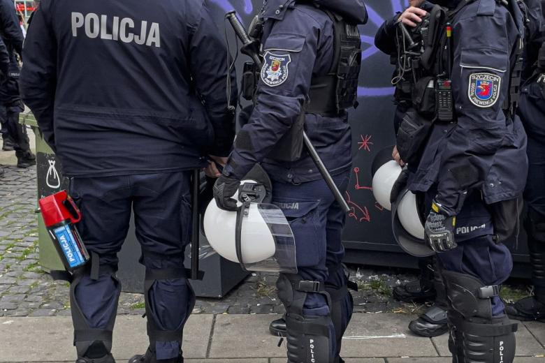 policjanci w kamizelkach, z hełmami, długimi pałkami i miotaczem gazu 
