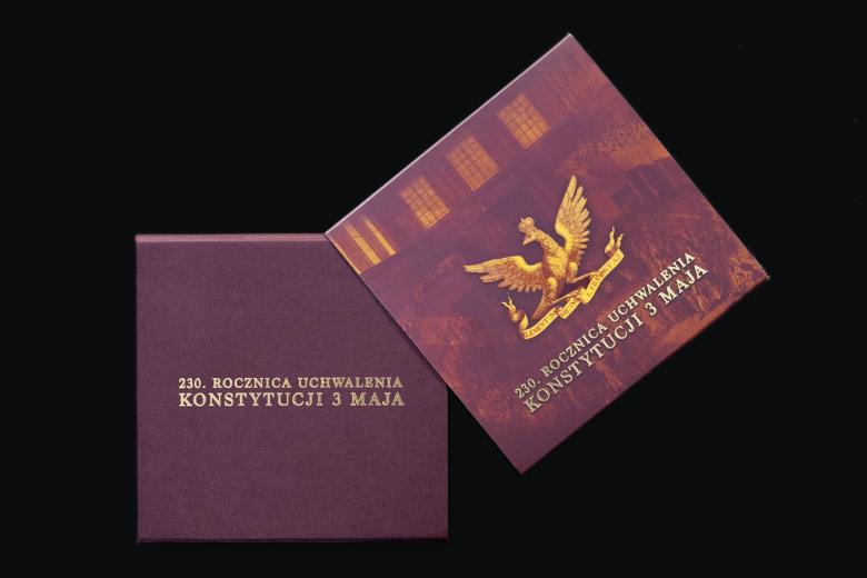 Bordowe pudełko i okładka ze złotym orłem i napisem 230. rocznica uchwalenia Konstytucji 3 maja