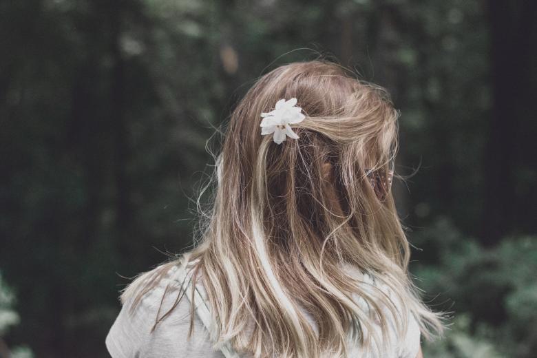 Siedząca tyłem dziewczynka z kwiatem w długich włosach