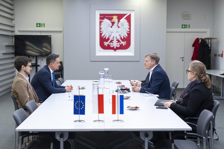 pięć osób siedzi po dwóch stronach stołu w sali konferencyjnej i rozmawia, w tle godło Polski, na pierwszym małe, stojące na stole flagi Polski, Holandii i Unii Europejskiej
