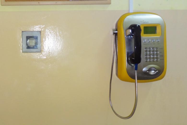 Aparat telefoniczny wiszący na ścianie obok włącznika światła w zakładzie karnym