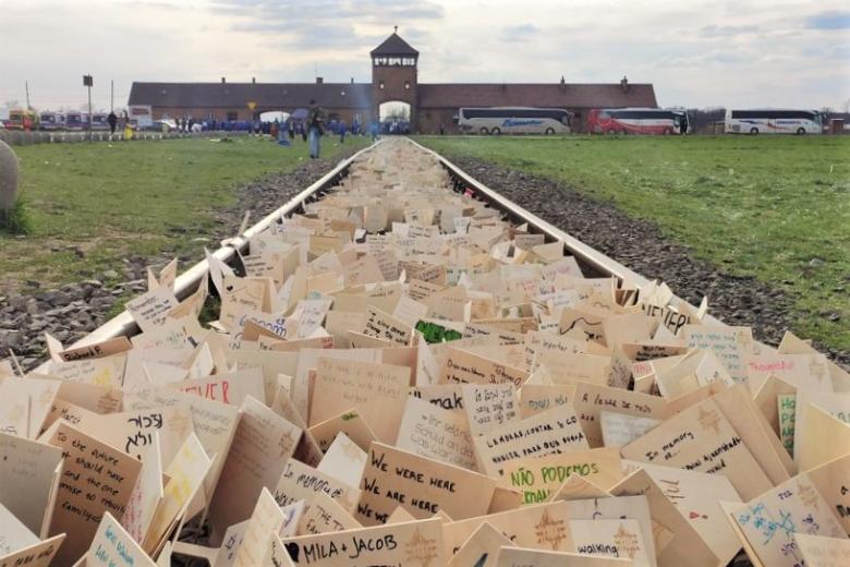 Tysiące małych karteczek powkładanych w podkłady kolejowe prostego toru, który biegnie w kierunku bramy zabudowań byłego obozu Auschwitz Birkenau