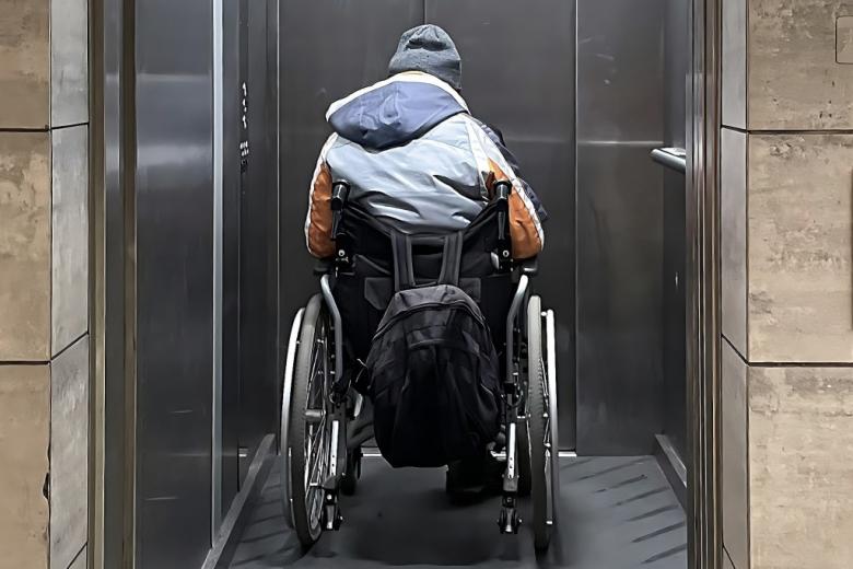 widziana od tyłu osoba z niepełnosprawnością na wózku w windzie