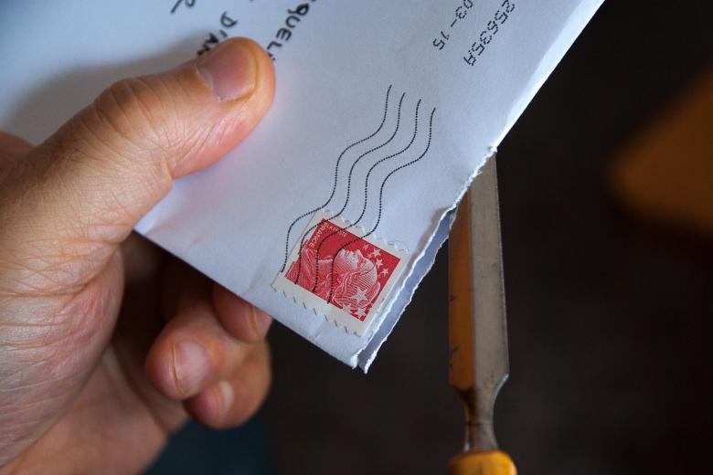 Dłoń trzymająca zamknięty list, który jest otwierany nożykiem