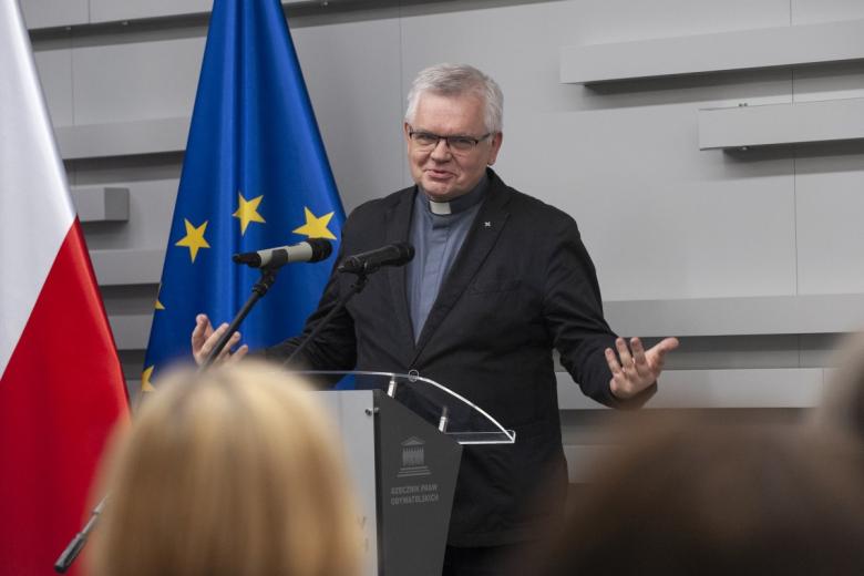 o. Hieronim Kaczmarek przemawia na tle flag Polski i UE
