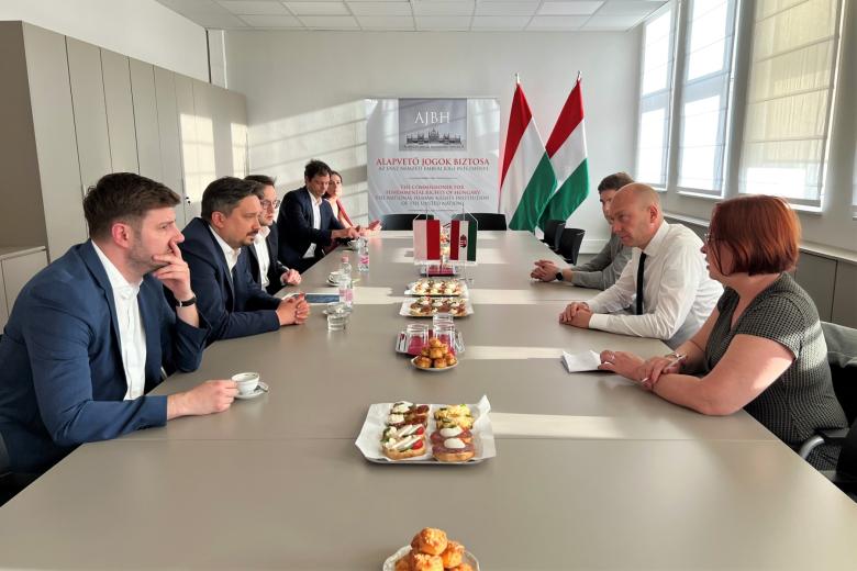Grupa osób siedzi po dwóch stronach dużego prostokątnego stołu, na stole stoją małe flagi Polski i Węgier