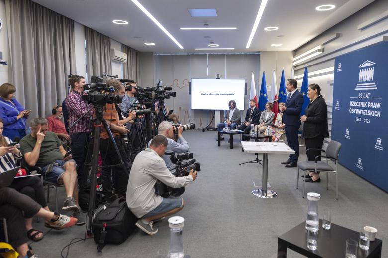RPO Marcin Wiącek stoi przed kamerami i mówi do mikrofonu, obok niego tłumacz polskiego języka migowego