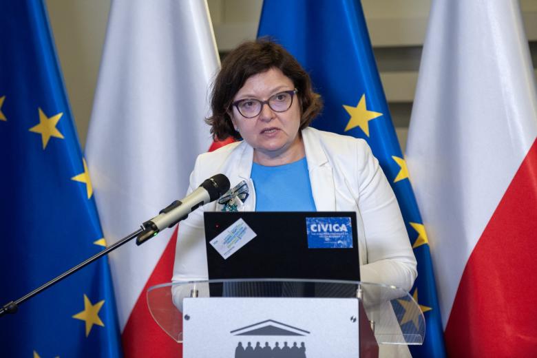 Agnieszka Chłoń-Domińczak przemawia za mównicą na tle flag Polski i UE