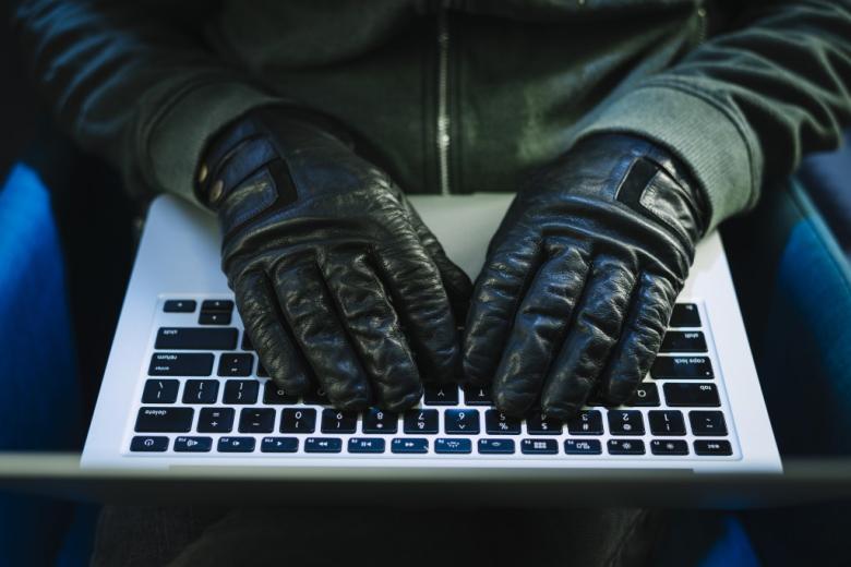 dłonie osoby w czarnych rekawiczkach na klawiaturze laptopa 