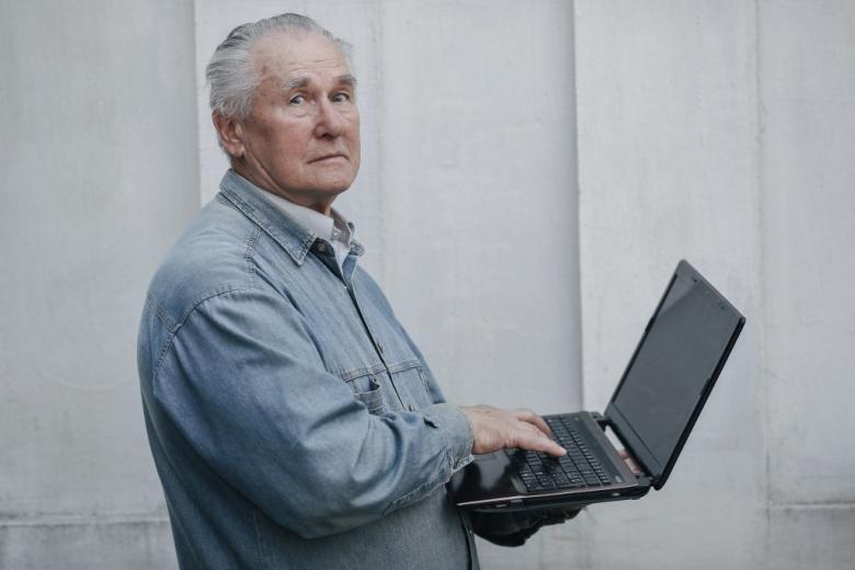 starszy mężczyzna trzyma w rękach otwartego laptopa