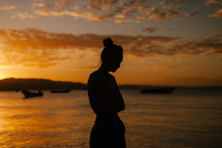 kobieta stoi nad morzem na tle zachodzącego słońca
