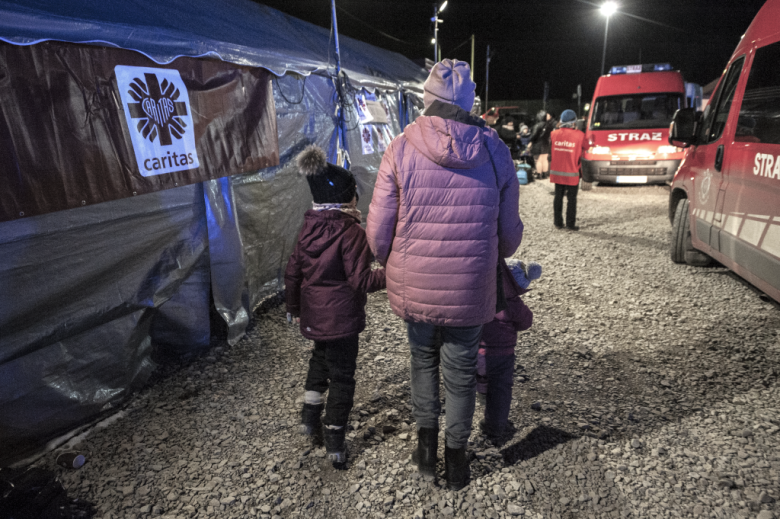 odwrócona tyłem kobieta z dwojgiem dzieci w punkcie dla uchodźców nocą 