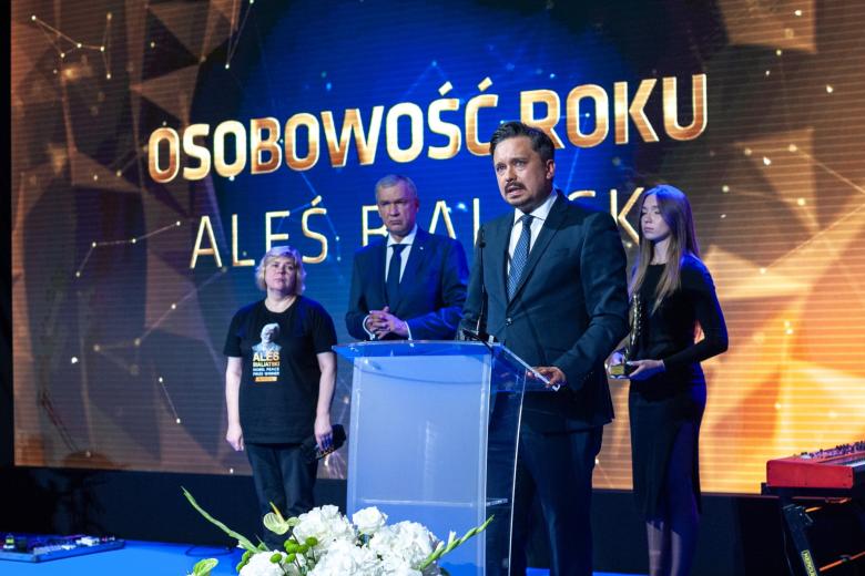 Marcin Wiącek przemawia za mównicą na scenie, w tle na wyświetlaczu napis "Osobowość Roku, Aleś Bialacki"