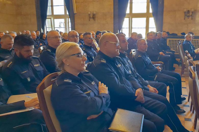 Kilkudziesięciu funkcjonariuszy Policji w mundurach siedzi na sali konferencyjnej i słucha wystąpienia