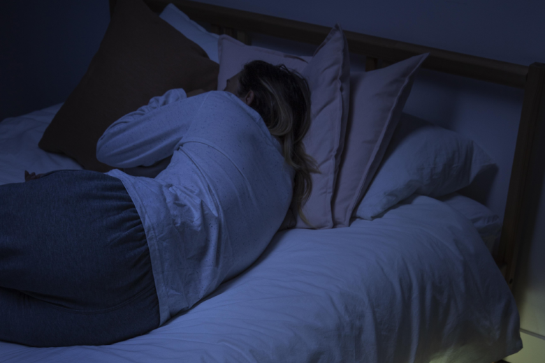 skulona kobieta leży odwrócona tyłem na łóżku w ciemnościach