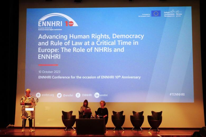 Kobieta za mównicą, w tle duży ekran z napisem po angielsku "ENNHRI’s 10th anniversary conference: Advancing human rights, democracy and rule of law at a critical time in Europe: the role of NHRIs and ENNHRI"