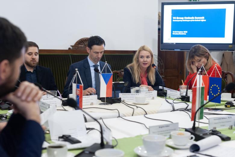 Trzy osoby siedzące za stołem, na którym stoi mała flaga Czech