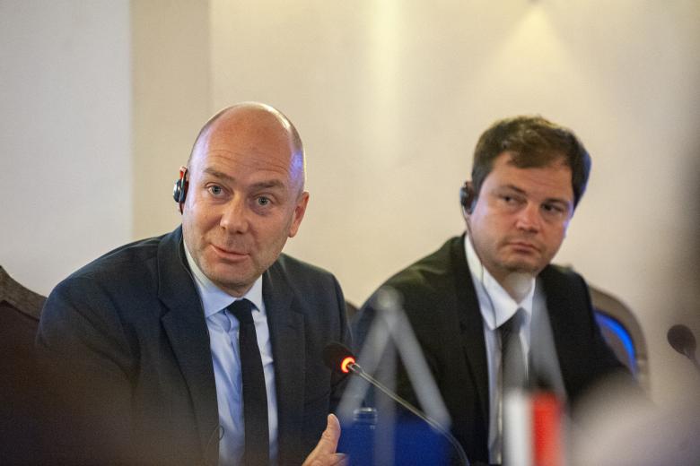 Dwie osoby siedzą przy stole. Obie mają po słuchawce w uchu. Jedna z nich - ombudsman Węgier - wypowiada się do mikrofonu.