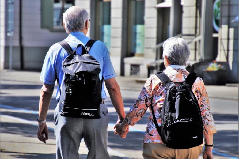 dwoje seniorów widzianych z tyłu trzyma się za ręce na ulicy