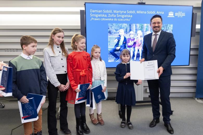 Marcin Wiącek pozuje do wspólnego zdjęcia z pięciorgiem dzieci trzymających dyplom