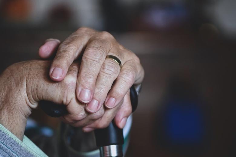 dłonie starszej osoby splecione na rękojeści  laski 