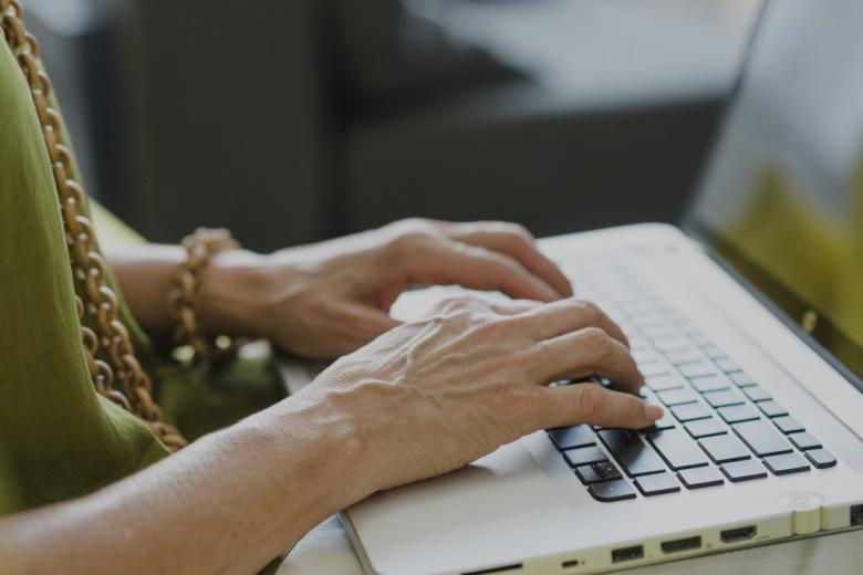 ręce starszej kobiety na klawiaturze laptopa