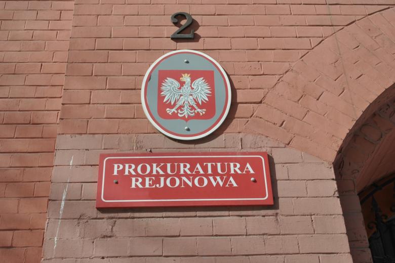 Czerwona tabliczka z napisem "Prokuratura Rejonowa" na ceglanym murze