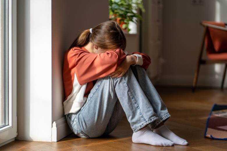 Smutna nastolatka siedzi na podłodze z głową schowaną w ramionach podpartych o kolana