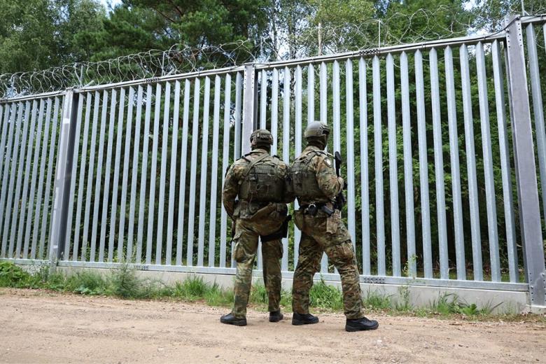 dwaj zołnierze stoją tyłem przy zaporze granicznej 