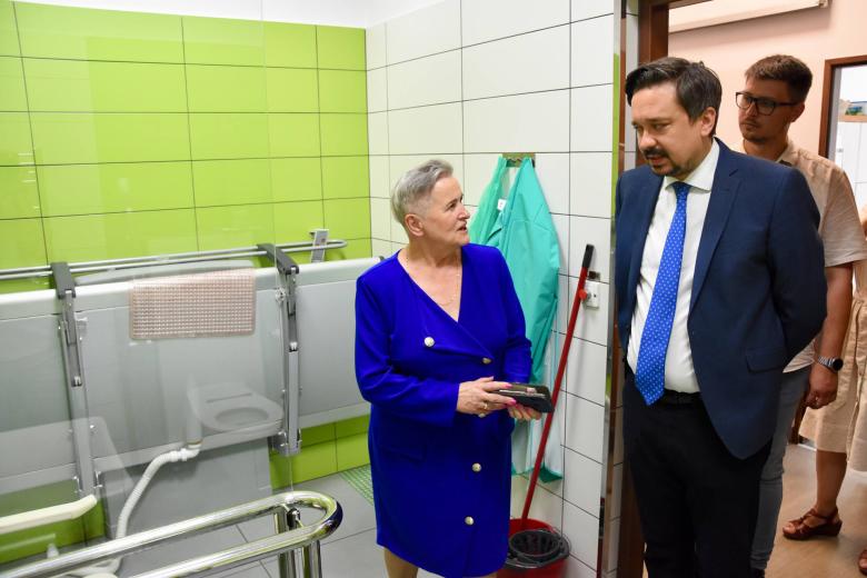RPO Marcin Wiącek rozmawia z prezes stowarzyszenia Alicją Szatkowską w toalecie dostosowanej do potrzeb osób z niepełnosprawnościami. Na ścianie toalety zamontowana jest składana komfortka.