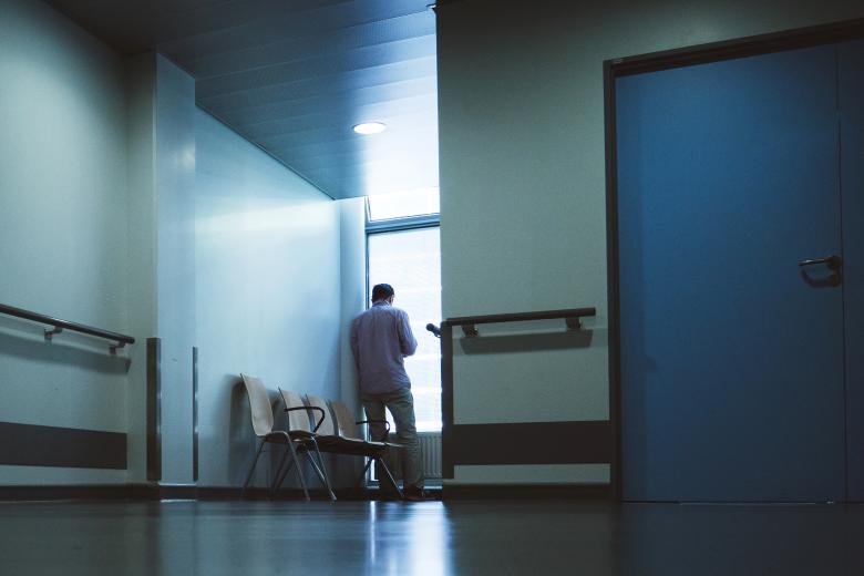 Samotny mężczyzna wygląda przez okno stojąc w ciemnym szpitalnym korytarzu