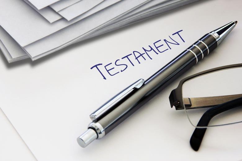 Kartka papieru z napisanym odręcznie nagłówkiem "Testament". Na kartce leżą długopis i okulary