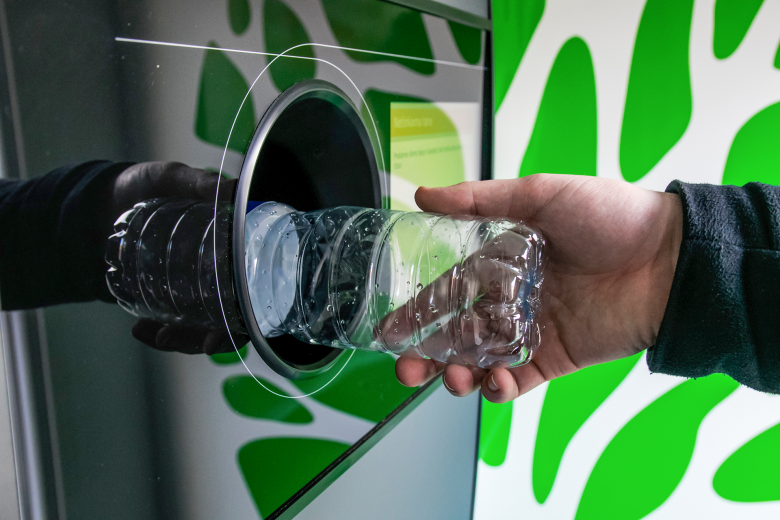 Dłoń osoby wkładająca plastikową butelkę do otworu w automacie
