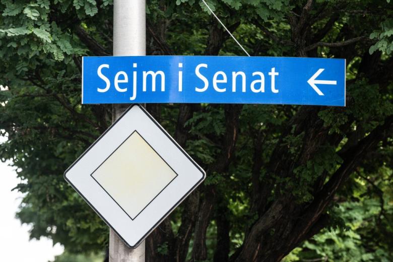 tablica na słupie wskazująca kierunek do Sejmu i Senatu 