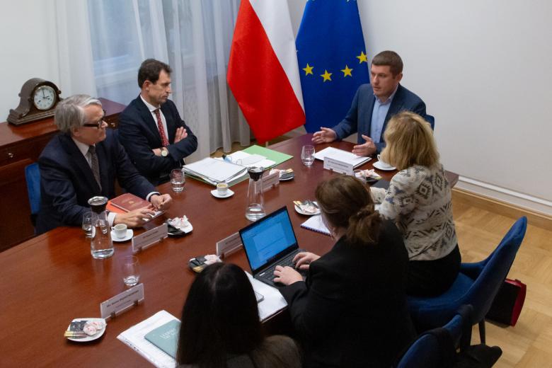 ZRPO Wojciech Brzozowski rozmawia z gośćmi przy konferencyjnym stole. W tle flagi Polski i Unii Europejskiej