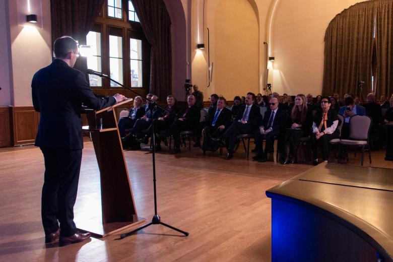 Prowadzący konferencję Maciej Kruk wypowiada się z podium w stronę publiczności.