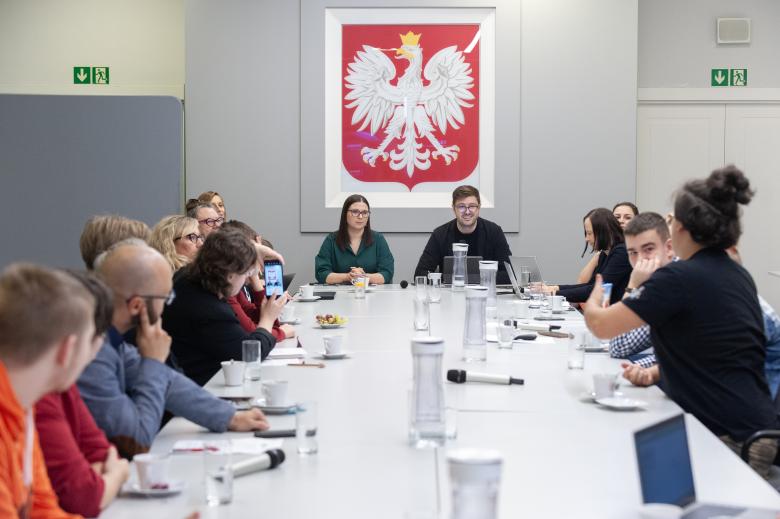 Valeri Vachev i kilkanaście innych osób rozmawiają przy stole konferencyjnym. W tle godło Polski