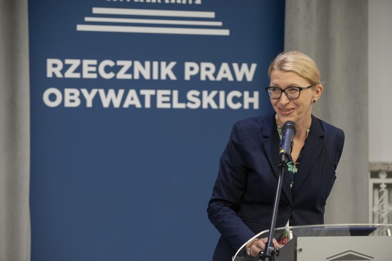 Paulina Malinowska-Kowalczyk uśmiechając się wypowiada się, stojąc przy mównicy