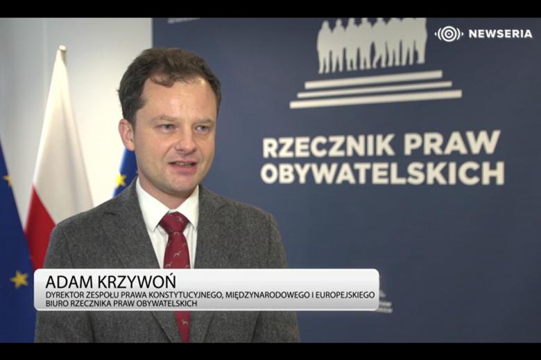 Osoba wypowiada się do kamery na tle ścianki z napisem "Rzecznik Praw Obywatelskich" i flag Polski i UE