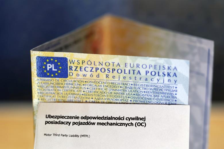 Zbliżenie na ustawiony na biurku blankiet polskiego dowodu rejestracyjnego pojazdu i kartonik z napisem "Ubezpieczenie odpowiedzialności cywilnej posiadaczy pojazdów mechanicznych (OC)"