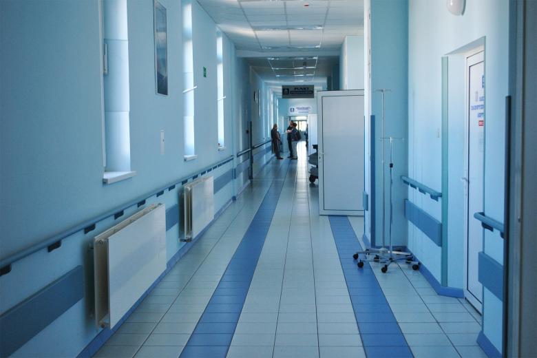 Ogólny widok długiego korytarza w szpitalu. Na końcu korytarza stoi rozmawiająca grupa ludzi