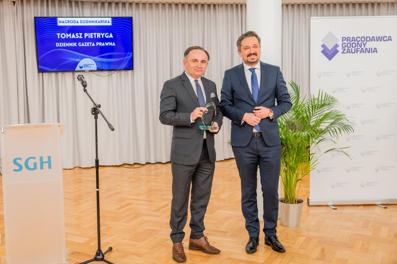 Marcin Wiącek i Tomasz Pietryga stoją i uśmiechają się, pozując do zdjęcia. Tomasz Pietryga trzyma w dłoniach statuetkę nagrody.