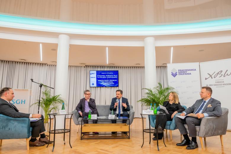 Pięć osób siedzi w ustawionych w półokrąg fotelach i dyskutuje.