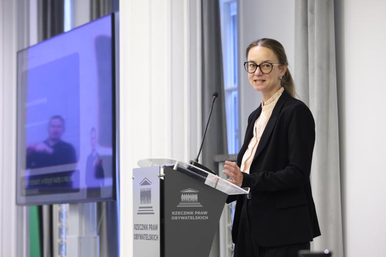 Hanna Kuczyńska wypowiada się stojąc przy mównicy w sali konferencyjnej
