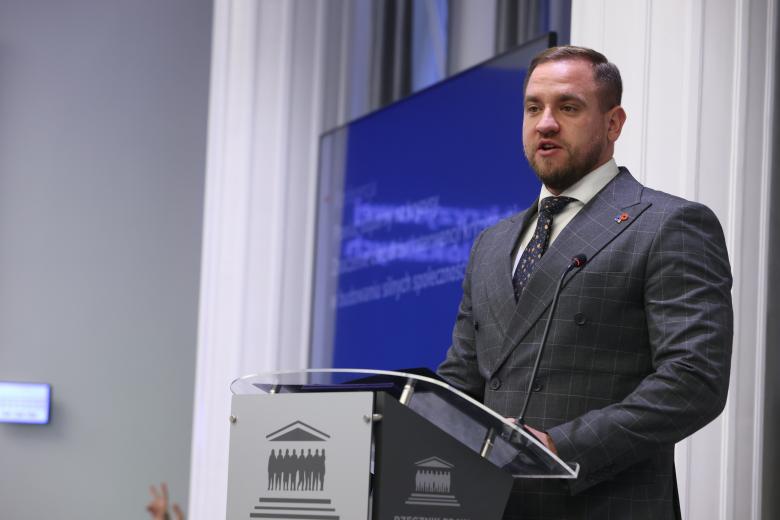 Adrian Ejssymont wypowiada się stojąc przy mównicy