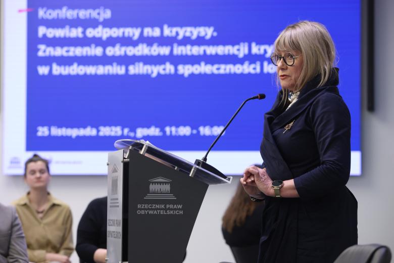 Katarzyna Wiśniewska wypowiada się stojąc przy mównicy.