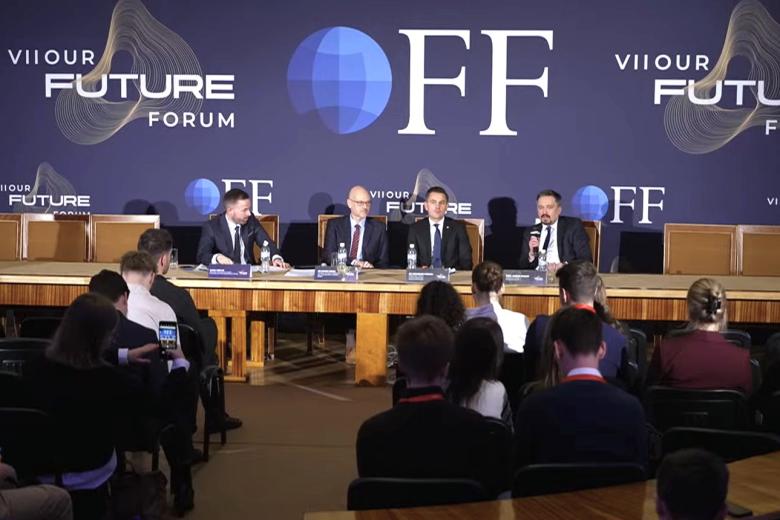 Cztery osoby siedzą za stołem w sali konferencyjnej, przysłuchuje się im kilkadziesiąt osób siedzących na sali