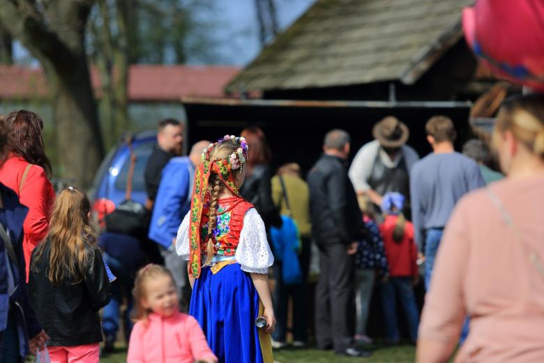 Tłum ludzi na imprezie na otwartym powietrzu. W centrum kadru widać kobietę w barwnym stroju ludowym